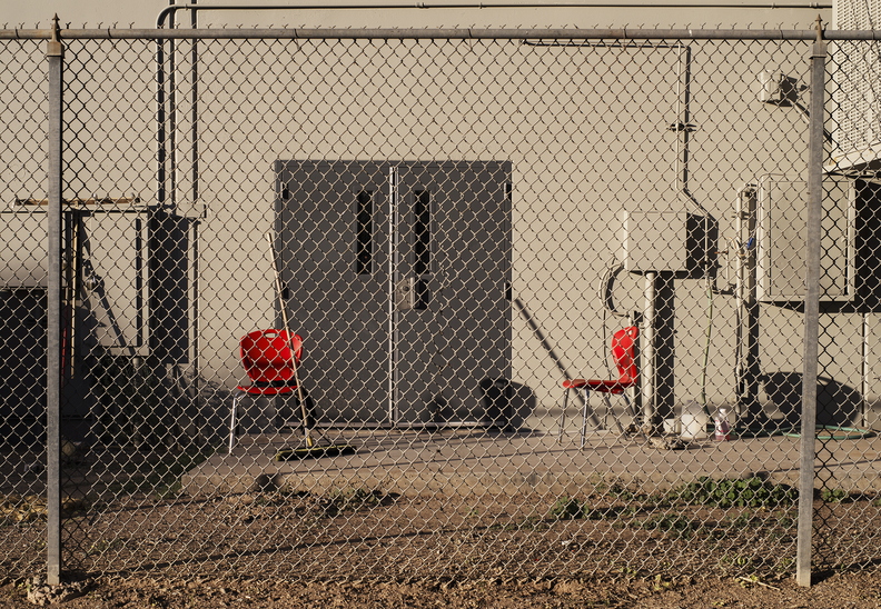 Two_red_chairs_broom_behind_wire_fence_01.jpg